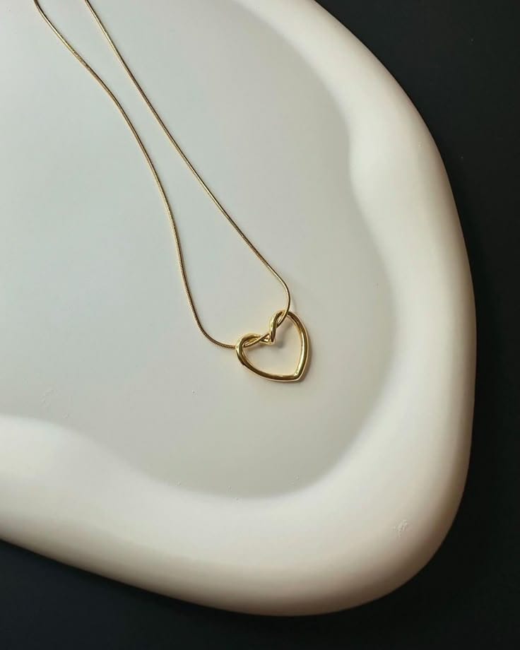 Gold heart-shaped necklace on a white dish with a black background