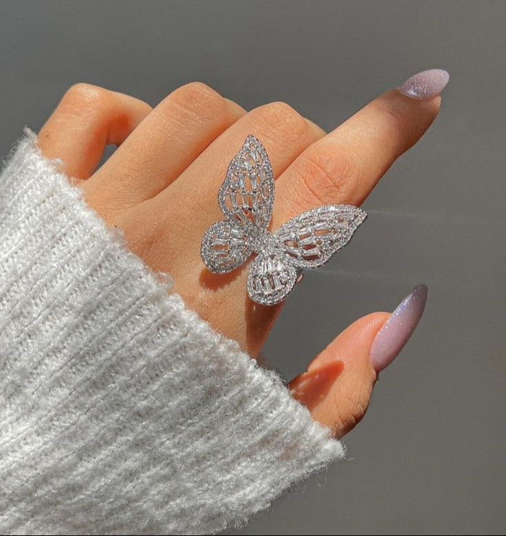 Silver butterfly ring on a finger with a gray background