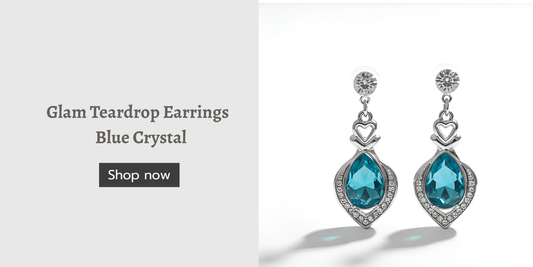 Pair of silver teardrop earrings with blue crystal gemstones and small heart accents, displayed on a white background next to text that reads ‘Glam Teardrop Earrings Blue Crystal