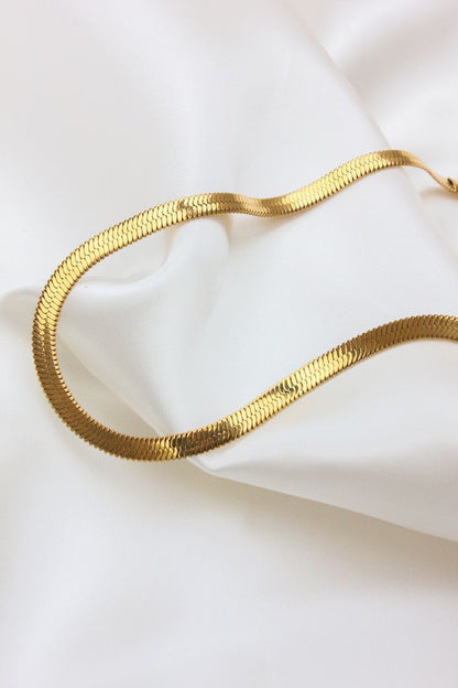 Gold snake-shaped necklace on a white fabric background