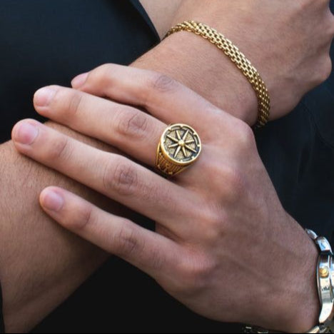 Gold necklace, bracelet, and ring on a person against a black background