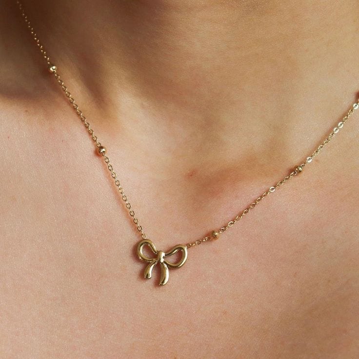 Gold necklace with a bow pendant on a person's neck