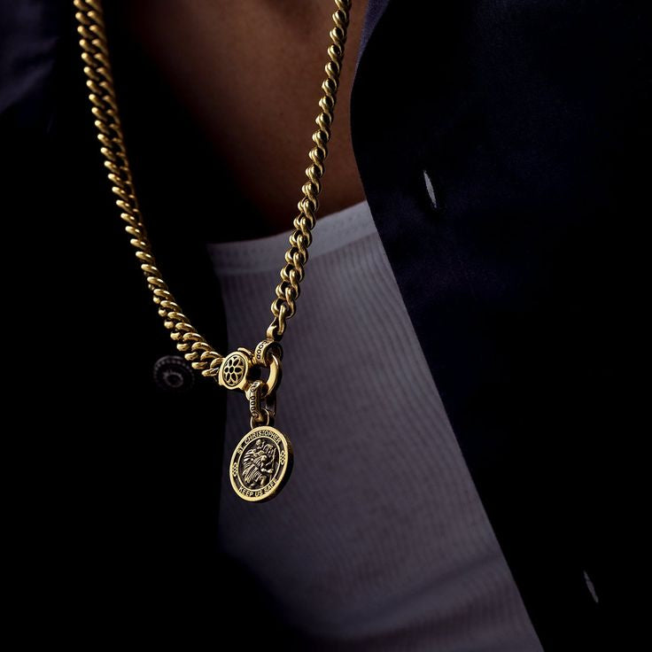 Gold chain necklace with a pendant on a person wearing a dark outfit.
