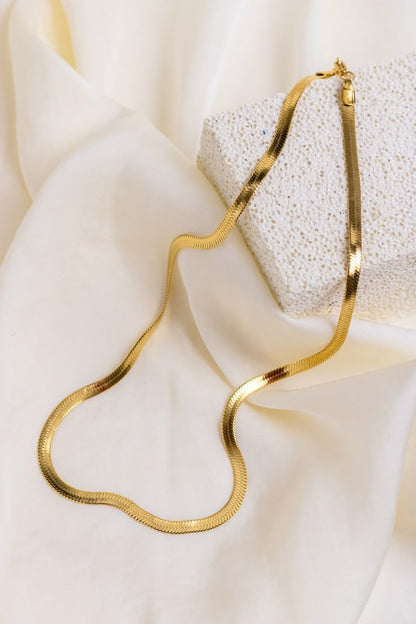Gold snake chain necklace on a white fabric background