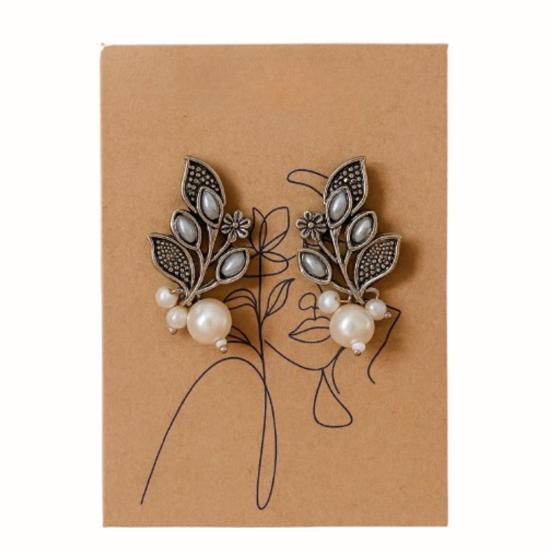 Pair of decorative earrings with leaf and pearl details on a brown card.