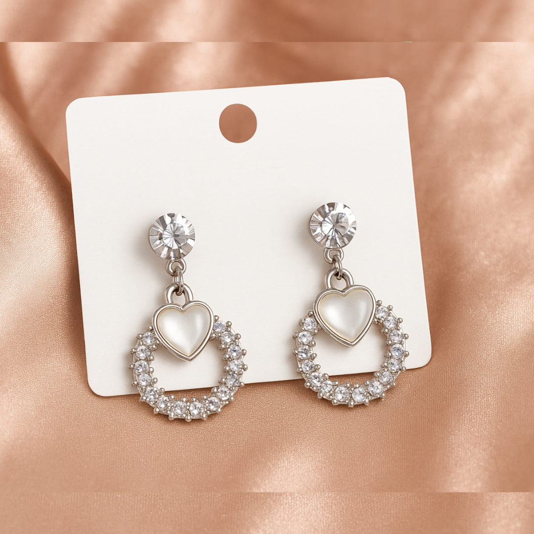 Heart-shaped earrings with clear stones on a white card against a pink satin background