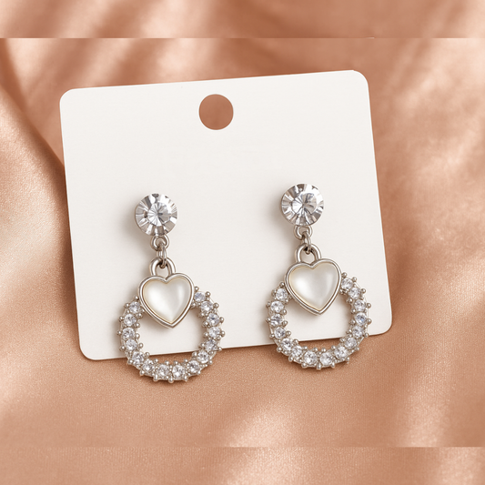 Heart-shaped earrings with clear stones on a white card against a pink satin background