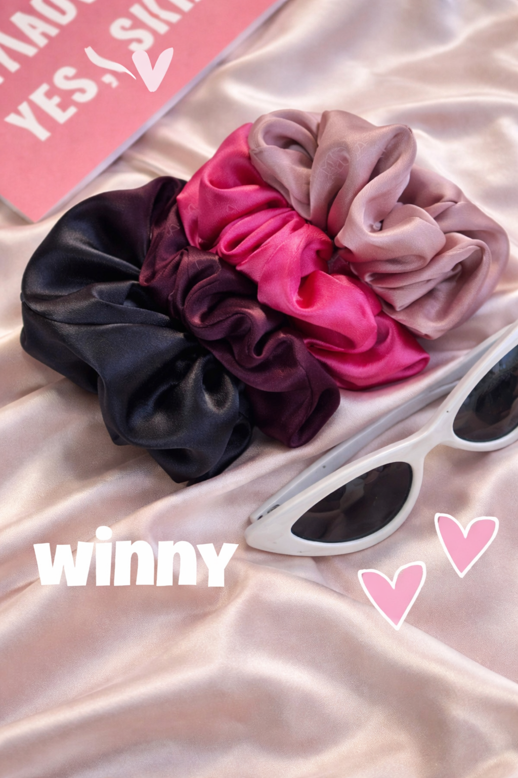 Three scrunchies in black, pink, and beige on a pink fabric background with 'winny' .